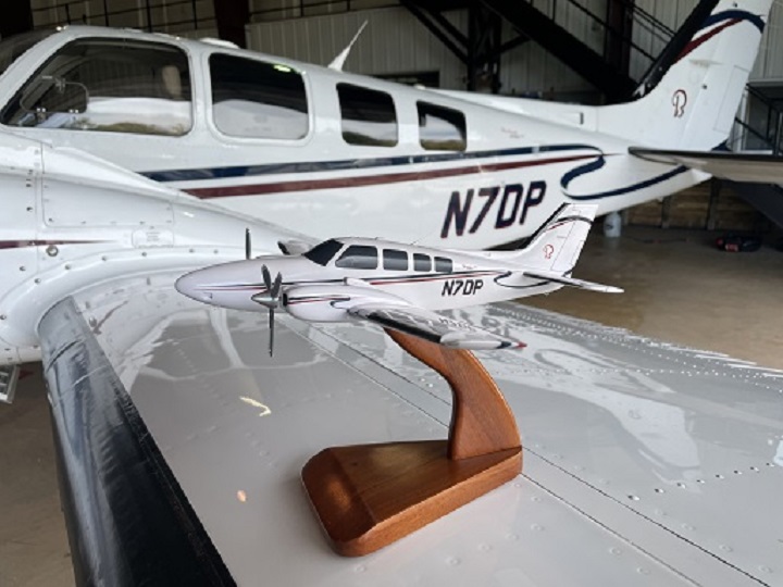 Beechcraft Baron G58 custom aircraft model on wooden stand beside real airplane with matching tail number N7DP