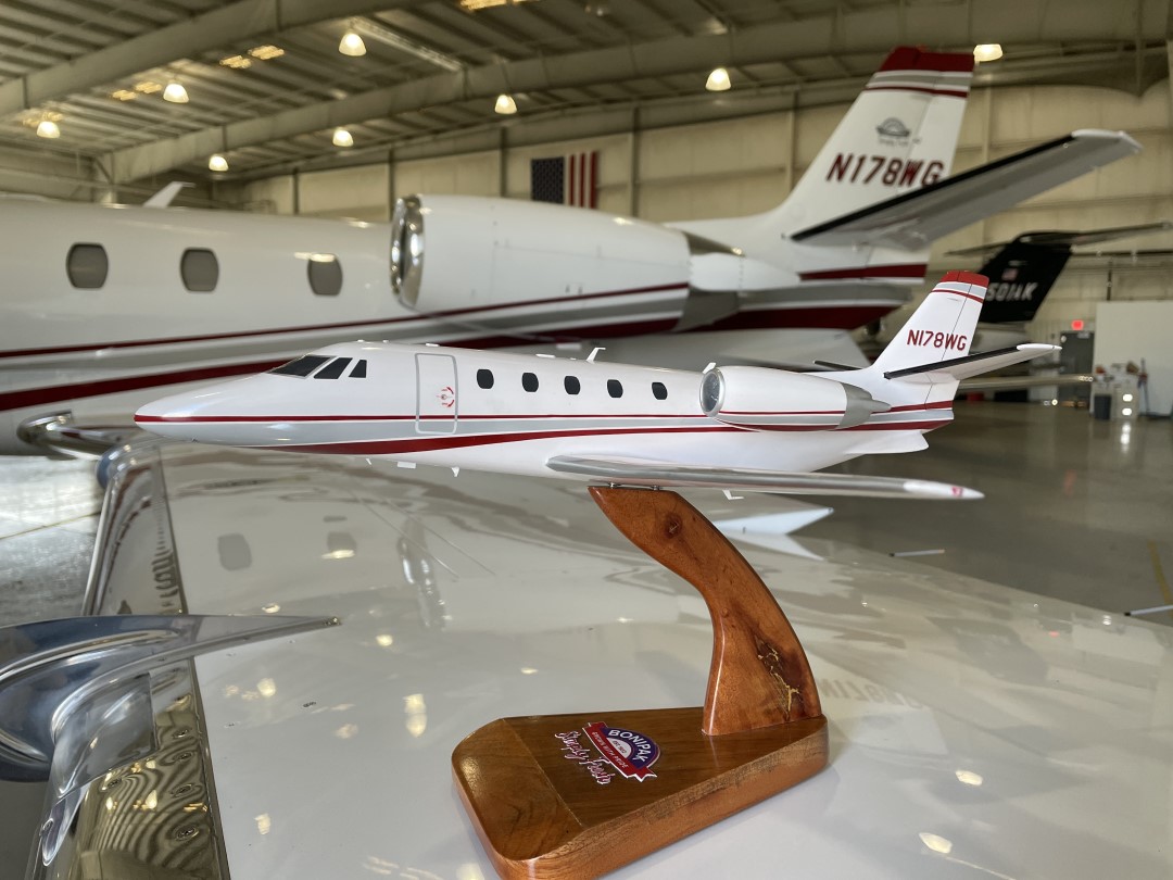 Cessna Citation XLS+ business jet model with tail number N178WG on wooden stand, shown in front of matching real jet in hangar