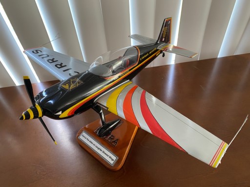 Extra 330LX model with black fuselage, red and yellow striped wings, and plaque text on wooden stand