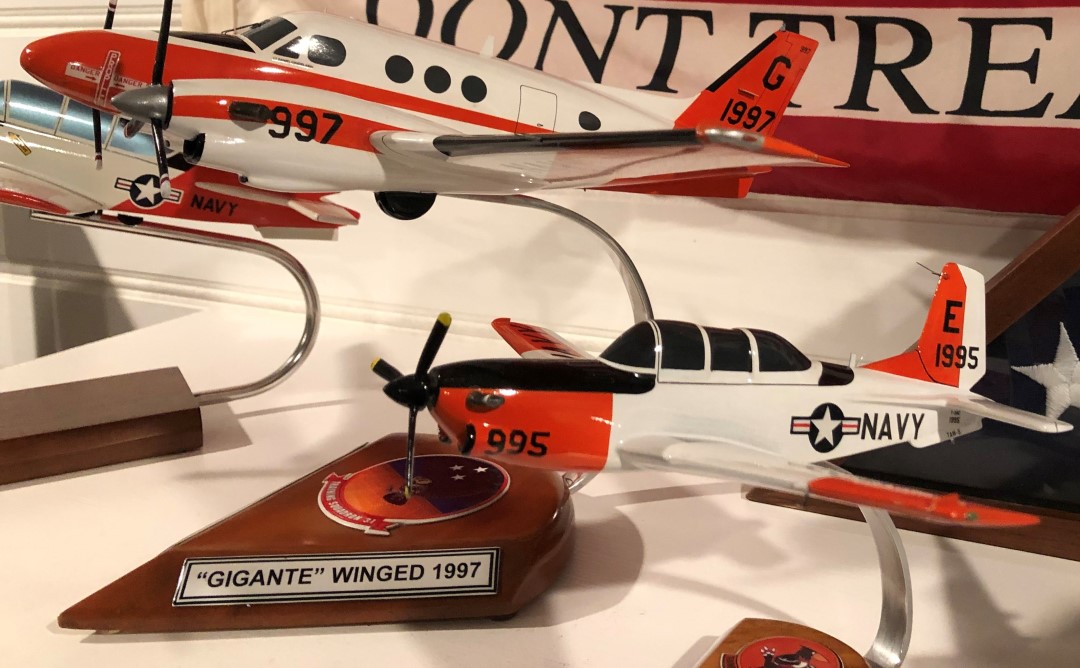 T‑44A and T‑34C mini aircraft models on curved metal stands with Navy markings displayed side by side