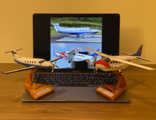 Miniature Pilatus PC‑12 and Cessna 208 Caravan models on stands in front of laptop showing real aircraft