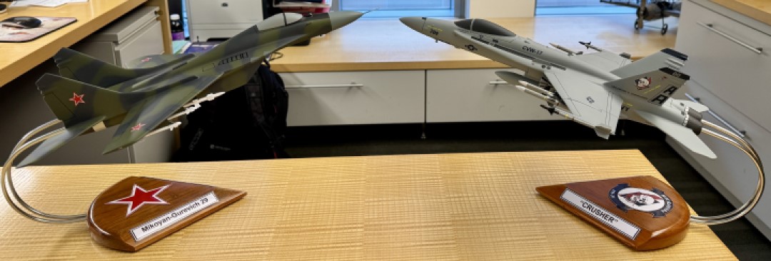 FA‑18C and MiG‑29 aircraft models on curved metal stands with camouflage and gray paint schemes displayed side by side