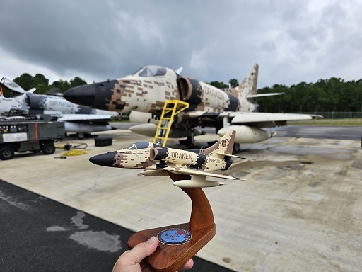 A‑4 Skyhawk model on wooden stand with desert camouflage and DRAKEN name, shown in front of matching jet