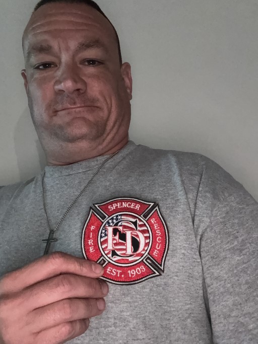 Person holding or wearing a gray shirt featuring the Spencer Fire Rescue embroidered Maltese cross patch with American flag design