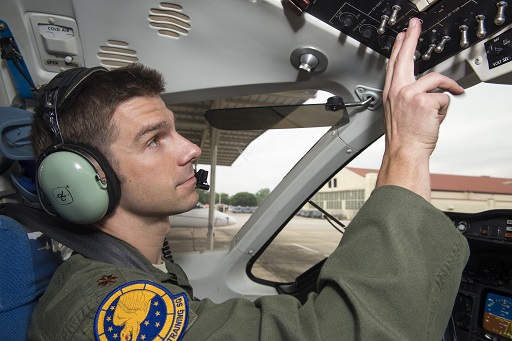 Pilot in flight suit operating cockpit controls, wearing 99 FTS Student Heritage Patch on sleeve