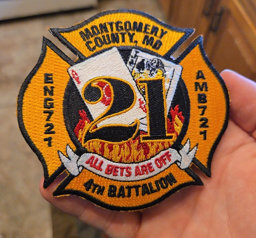 Hand holding Montgomery County Fire and Rescue Service patch with embroidered flames, cards, and unit details