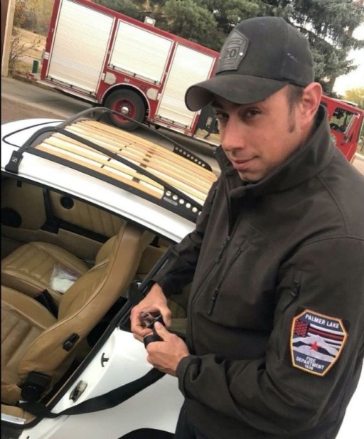 Firefighter wearing Palmer Lake Fire Department Thin Red Line patch with fire truck in background symbolizing pride and unity among first responders