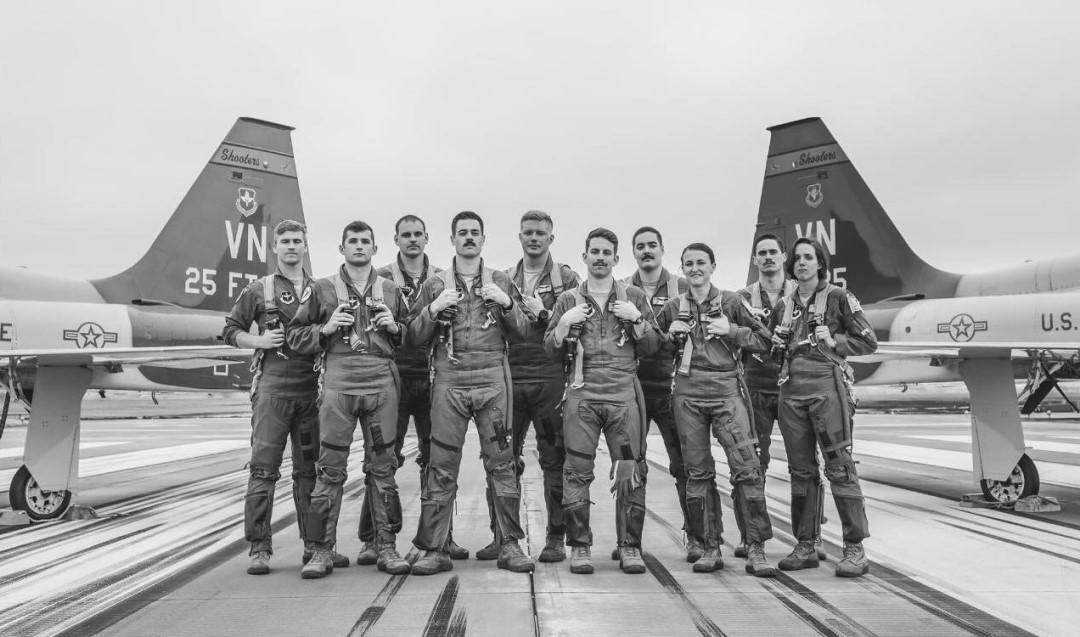 Group of 25th Flying Training Squadron Airmen in flight suits standing on airfield in front of T‑38 aircraft