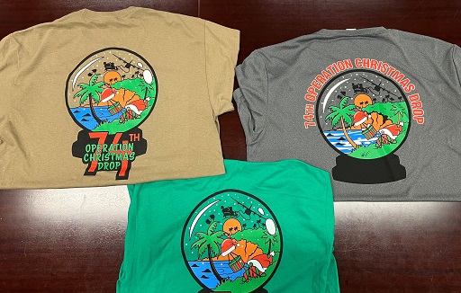 Three 74th Operation Christmas Drop shirts laid out showing colorful holiday-themed back designs