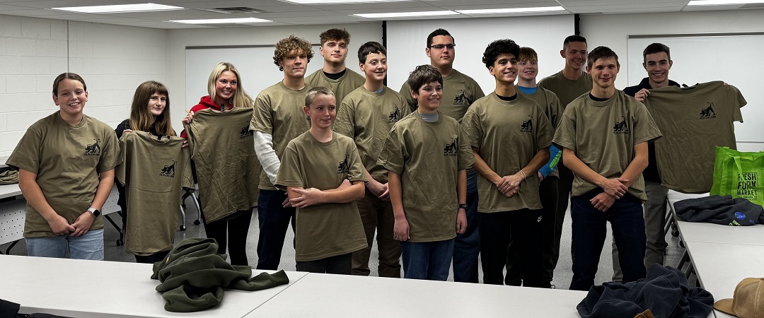 Group wearing GLR-OH-096 CAP shirts in classroom; some hold shirts, others pose for photo