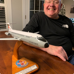 gallery image of satisfied customer with large smile sitting next to us air force aircraft model mounted to wooden stand