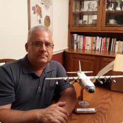 gallery image of retired service customer sitting next to a replica aircraft model