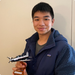 gallery image of young satisfied customer holding miniature aircraft model mobnted to wooden stand